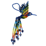 A handmade beaded hummingbird ornament featuring a blue and rainbow body and wings with multicolored accents, and long trailing strands of beads the colors of the rainbow on a plain white background.
