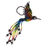A colorful beaded hummingbird ornament on a plain white background. The bird features a vibrant rainbow gradient on its body and wings, burgundy-purple seed bead details, and long trailing beaded tails with rainbow color beads.