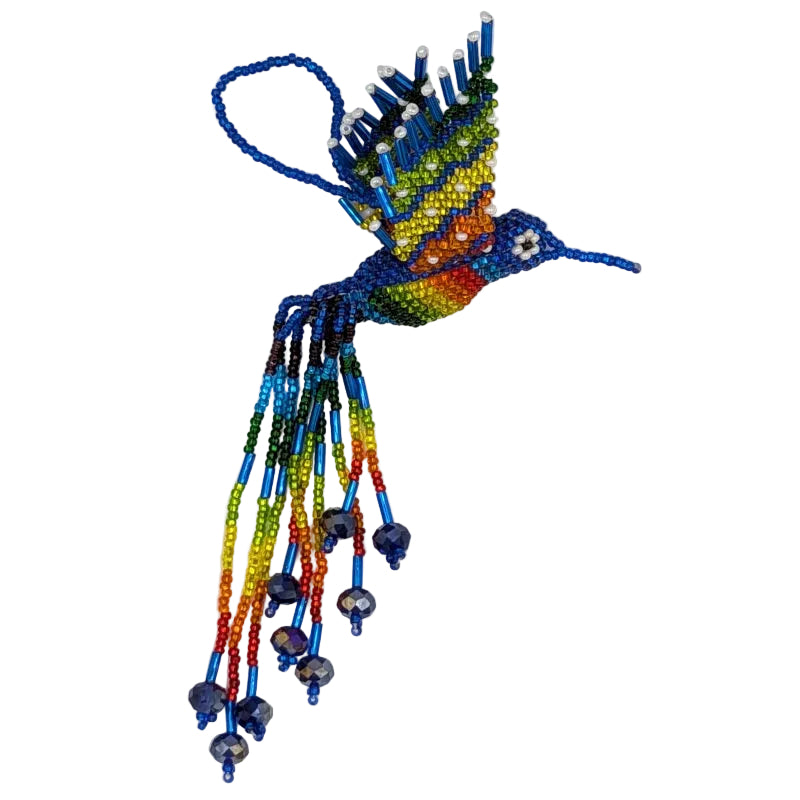 A handmade beaded hummingbird ornament featuring a blue and rainbow body and wings with multicolored accents, and long trailing strands of  beads the colors of the rainbow on a plain white background.