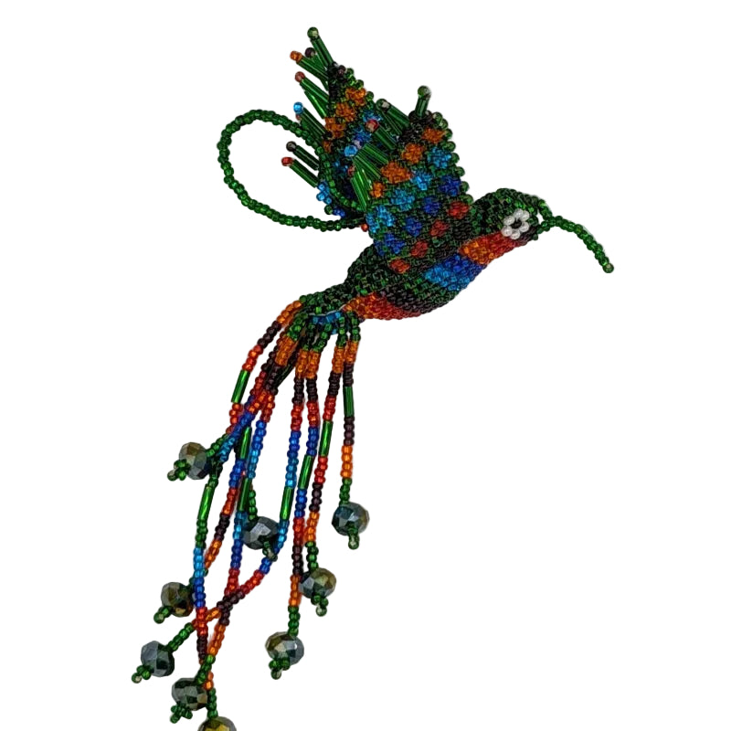 A handmade beaded hummingbird ornament featuring a vibrant mix of green, blue, red, and orange seed beads, with long trailing strands and iridescent bead accents, photographed on a plain white background.