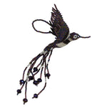 A beaded hummingbird ornament  featuring iridescent purple, purple, and silver white seed beads with a white eye detail, photographed on a plain white  background.