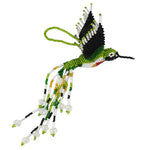 A hand-beaded hummingbird ornament on a plain white background. The design features green, black, white, and small red and yellow accents, with glass beads forming long flowing tails and a small hanging loop at the top.