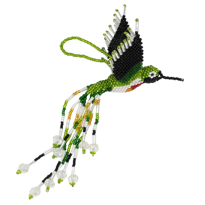A hand-beaded hummingbird ornament on a plain white background. The design features green, black, white, and small red and yellow accents, with glass beads forming long flowing tails and a small hanging loop at the top.
