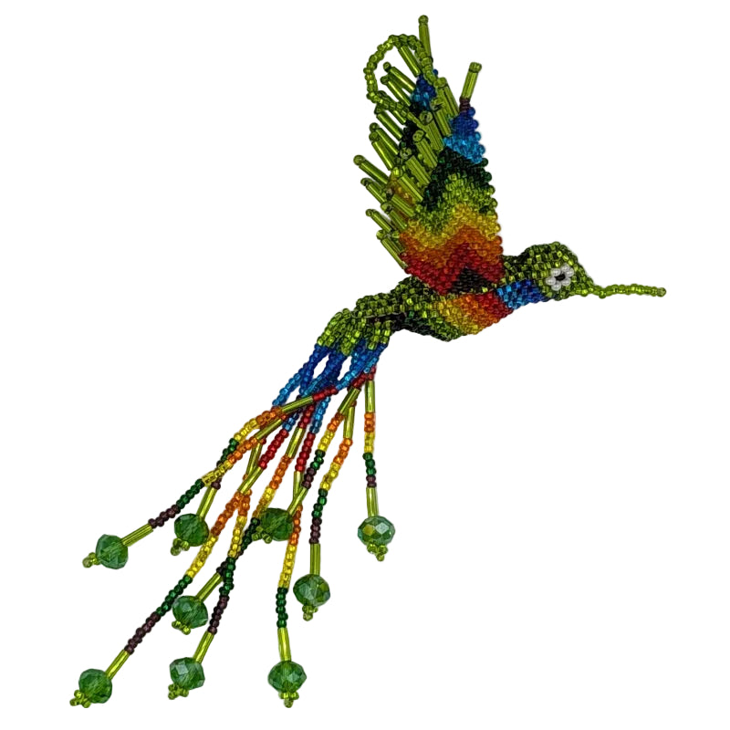 A handmade beaded hummingbird ornament, featuring a vibrant rainbow body and wings with dangling rainbow beaded tails with green crystals, photographed on a plain white background.