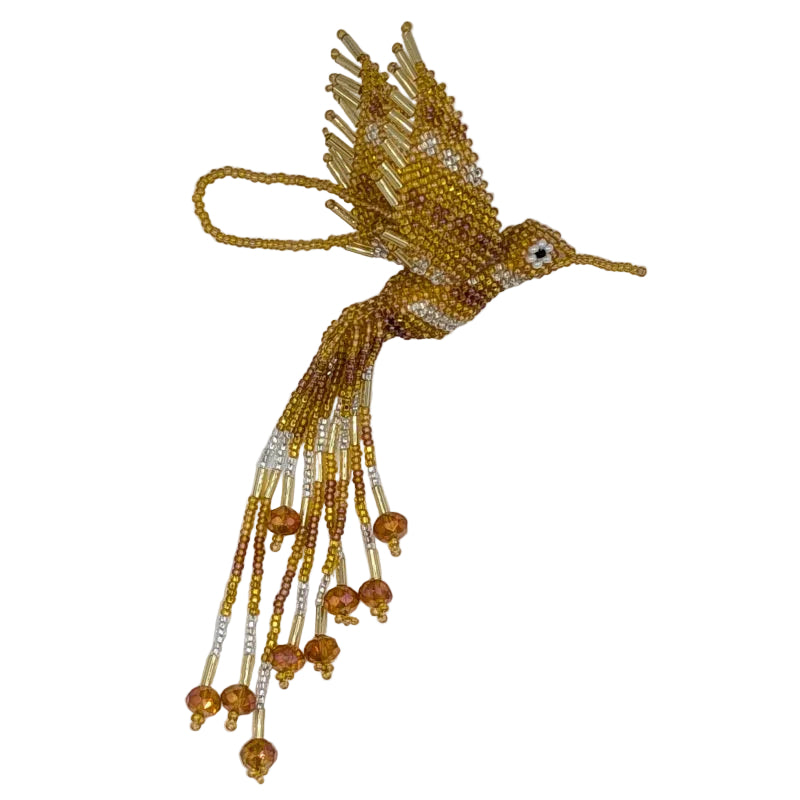 A handmade beaded hummingbird ornament, crafted with gold, amber, and white seed beads, featuring dangling bead strands and a small white eye detail, set against a plain white background.
